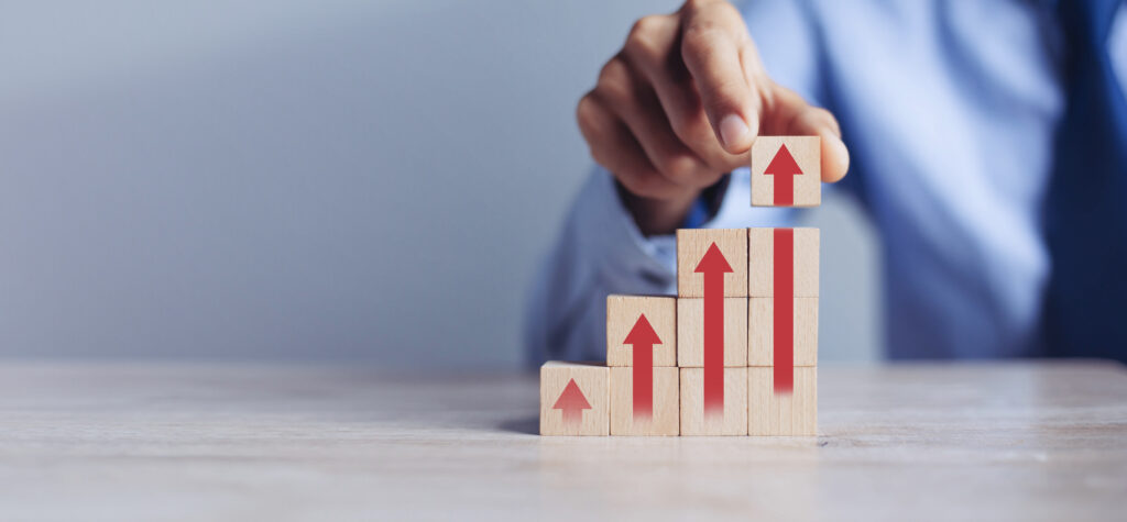 A hand stacks wooden blocks with red arrows pointing upward, forming a rising bar chart. The image symbolizes business growth, upward financial trends, and the importance of clean financial records in increasing valuation and buyer confidence.