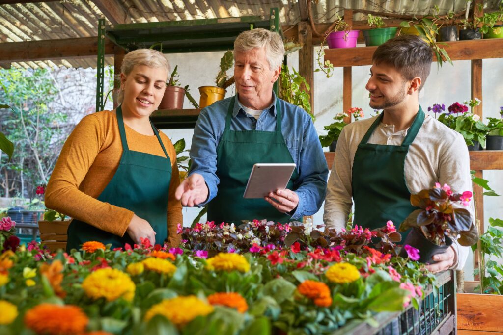 Older business owner in a greenhouse discussing operations with two younger employees, symbolizing a potential internal business sale to loyal team members.