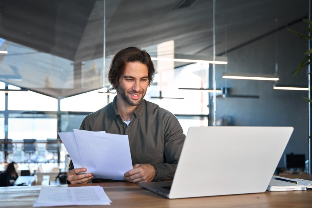 A confident business buyer reviews acquisition financing options at his desk, analyzing deal documents and funding strategies with a smile—ready to structure the right capital stack for a successful business purchase.