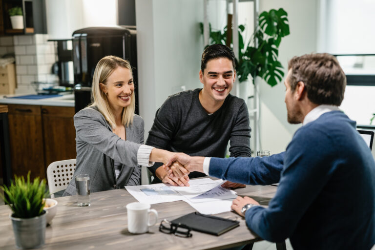 Smiling entrepreneurs shaking hands with a business advisor after securing SBA-backed financing to fund their business acquisition.