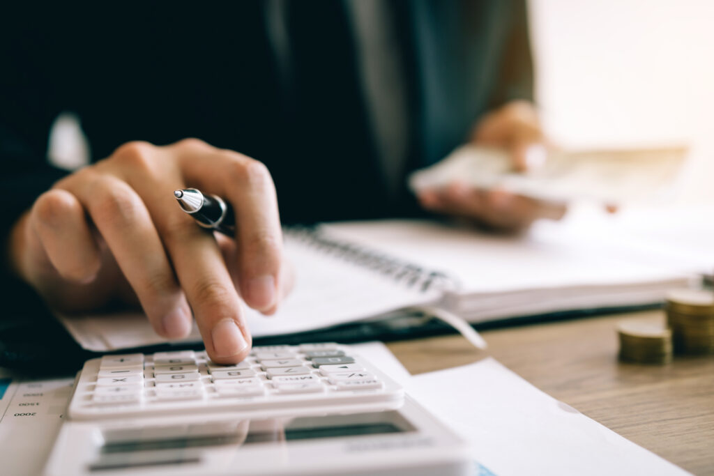 Close-up of a business owner using a calculator with financial documents, pen in hand, and cash in the background—symbolizing the importance of improving EBITDA, tracking financials, and preparing core metrics to maximize business value before sale.