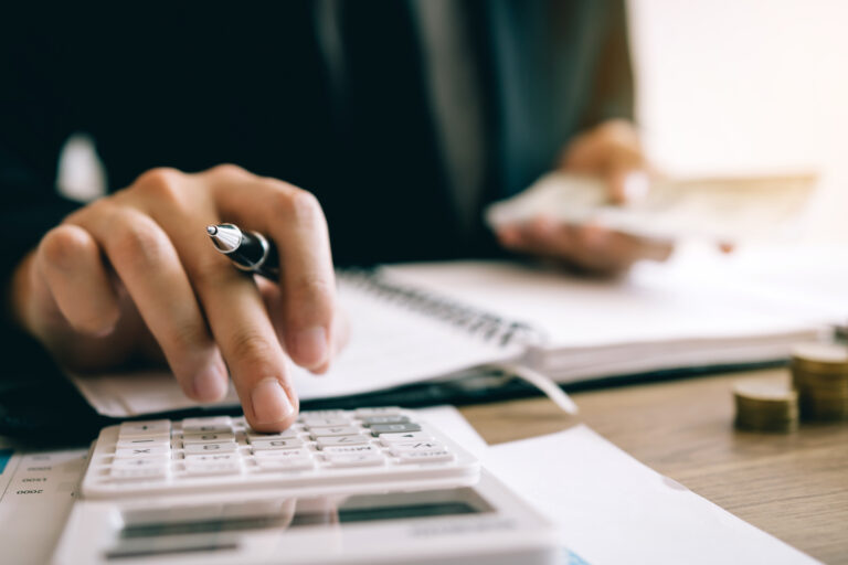 Close-up of a business owner using a calculator with financial documents, pen in hand, and cash in the background—symbolizing the importance of improving EBITDA, tracking financials, and preparing core metrics to maximize business value before sale.
