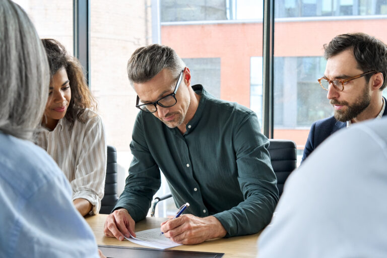 A serious business owner signs documents at a conference table, surrounded by advisors, symbolizing the critical process of selecting the right buyer to carry forward a business legacy.