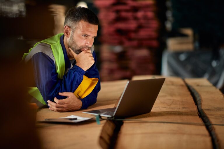 Blue-collar business owner or operations manager reviewing financial and operational data on a laptop inside a warehouse, representing seller financing risk analysis, business valuation strategy, and lower middle market business sales.